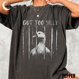 以下が含まれることがあります： ダークグレーのTシャツ。檻の向こうにアヒルのグラフィックと白い文字で「GOT TOO SILLY」と書かれています。 ヴィンテージ感のあるデザインです。