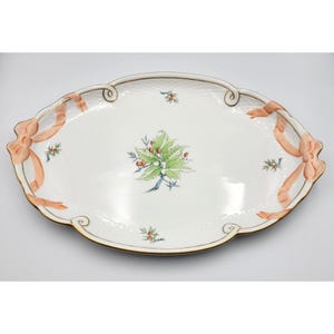 May include: An oval white porcelain serving platter featuring a central green leaf and orange berry motif. The rim is decorated with sculpted peach-colored ribbons and gold trim, with a subtle embossed basketweave texture on the border.