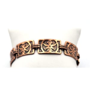 Puede incluir: Una pulsera de color cobre con eslabones rectangulares. Cada eslabón presenta un diseño simétrico detallado. La pulsera se muestra sobre una superficie blanca, mostrando su intrincada artesanía y cálidos tonos metálicos. Es una pieza de joyería.