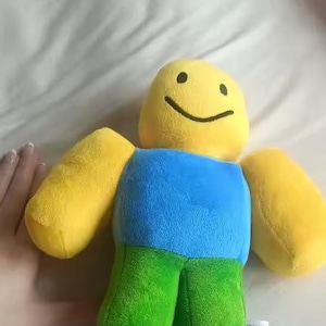May include: A plush toy in the shape of a character with a yellow head and arms, a blue torso, and green legs. The character has a simple, smiling face. The toy is soft and appears to be made of fabric.