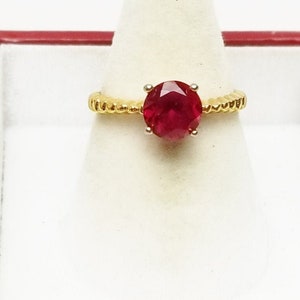May include: A gold ring with a red gemstone. The ring has a twisted band.