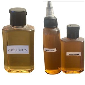 May include: Three bottles of liquid with black caps and white labels. The largest bottle has the text "GRES KOULEV" on the label. The other two bottles have the text "Bwa Anaconda" on the labels. The liquid is amber in color.