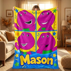 May include: A fleece blanket featuring four panels of the purple dinosaur character Barney against a bright yellow background, decorated with colorful stars and the name Mason printed in large yellow letters on a blue border at the bottom.