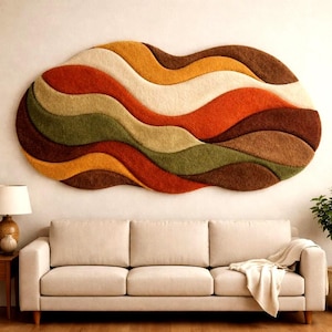 May include: A large, abstract wall hanging with a wavy design in shades of brown, orange, yellow, green, and cream. The textured piece is mounted above a beige sofa in a living room setting. The rug is approximately 72 inches wide.