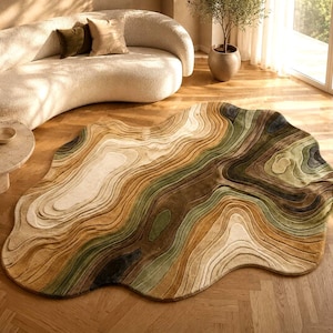 May include: An irregular, organic-shaped area rug featuring a layered, topographical map design. The rug displays a palette of earthy tones including shades of sage green, deep olive, warm tan, cream, and dark brown, with carved, textured contours.