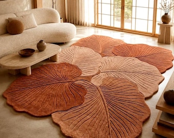 May include: A large area rug shaped like a cluster of overlapping leaves in varying shades of terracotta, rust, and beige. The rug features a textured surface with carved lines that mimic the veins of a leaf, creating a layered botanical design.