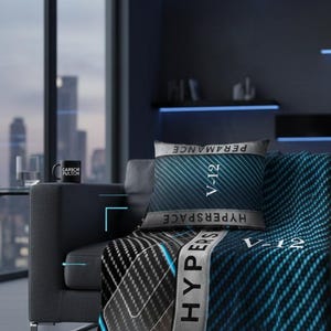 Può includere: Una scena di soggiorno moderno con un divano grigio con una coperta fantasia e un cuscino abbinato. La coperta e il cuscino hanno un design blu e nero con il testo "HYPERSPACE" e "V-12". Una tazza nera con testo bianco è su un tavolino.