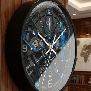 Peut inclure: Une horloge murale ronde avec un cadre noir et un cadran complexe à plusieurs niveaux, agrémenté d'accents bleus et de fibre de carbone. Le cadran affiche des chiffres blancs à 12, 3, 6 et 9, des aiguilles blanches et le texte CAG, LONGRA, SWISS MADE.