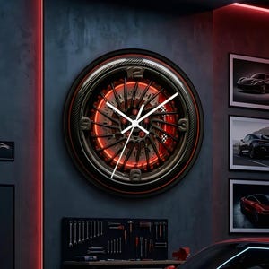 May include: A circular wall clock designed to resemble a car wheel rim with a dark metallic finish, featuring a central brake rotor illuminated by a red glow, white clock hands, and numerical markers at the twelve, three, six, and nine positions.
