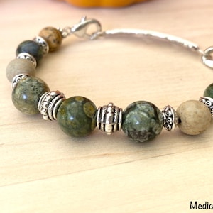 May include: A green and brown stone bracelet with silver accents. The bracelet has a clasp closure and is made with natural stones.