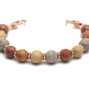 May include: A bracelet made of brown, beige, and gray patterned beads with rose gold accents.
