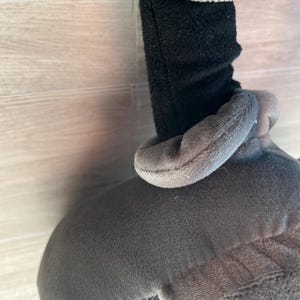 May include: A plush toy featuring a gray body and gloves, with a black sleeve. The toy has a soft, textured appearance. The gloves and head are a lighter shade of gray.
