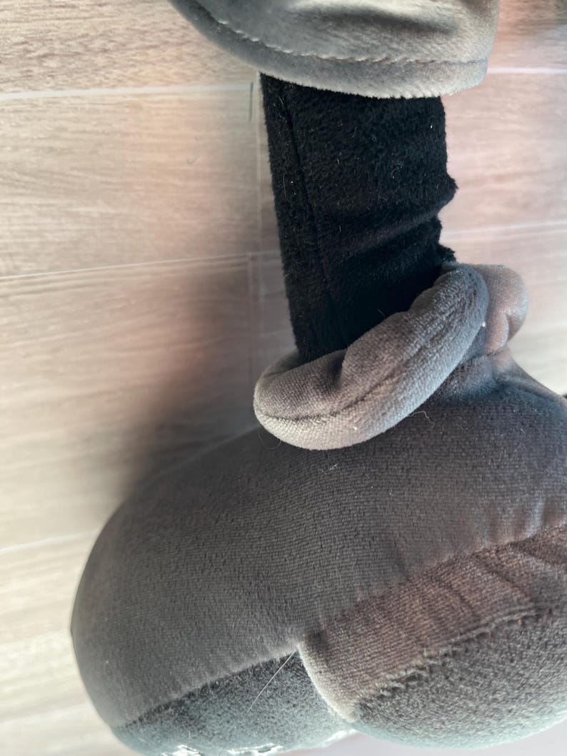 May include: A plush toy featuring a gray body and gloves, with a black sleeve. The toy has a soft, textured appearance. The gloves and head are a lighter shade of gray.