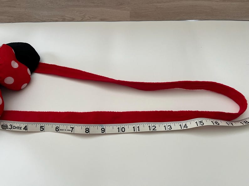 May include: A red headband with a black bow and a red bow with white polka dots. The headband measures approximately 18 inches in length. The bow is a classic design, perfect for themed parties or everyday wear.