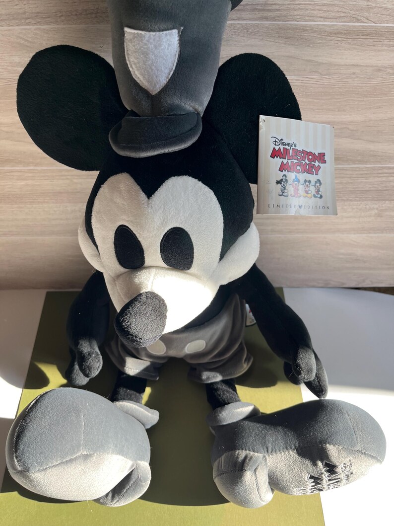 May include: A plush Mickey Mouse toy in black, white, and gray, with a hat and shorts. The toy has large ears and a tag that reads "Disney's Milestone Mickey Limited Edition."