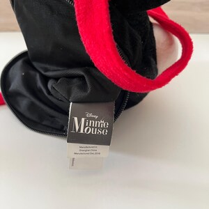 May include: Black plush Minnie Mouse purse with red handles. The purse has a zippered closure and a tag that reads "Minnie Mouse" and "Manufactured in Shanghai China Manufactured Dec.2018".