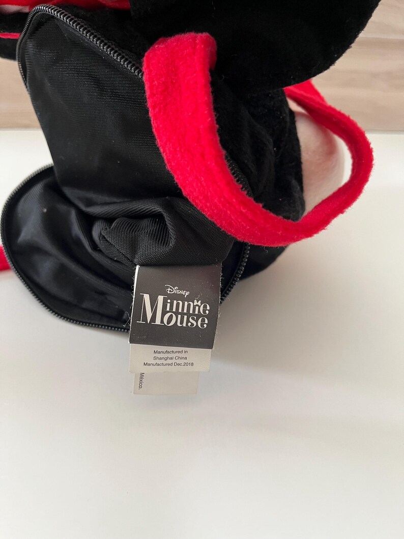May include: Black plush Minnie Mouse purse with red handles. The purse has a zippered closure and a tag that reads "Minnie Mouse" and "Manufactured in Shanghai China Manufactured Dec.2018".