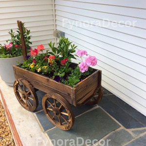 May include: A wooden wagon planter filled with colorful flowers. The planter has four spoked wheels and a dark brown finish. The flowers include pink, red, yellow, and purple blooms, creating a vibrant display for outdoor decor.