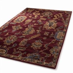 May include: A rectangular area rug featuring a deep burgundy background with a repeating pattern of stylized floral and geometric motifs in shades of gold, blue, and tan. The rug has a decorative border with a repeating linear pattern.