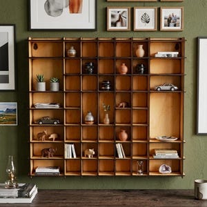 May include: A large, square wooden wall shelf with a grid of multiple open compartments. The light-colored wood structure features dark brown edges and contains various small decorative items, including miniature cars, vases, books, and figurines.
