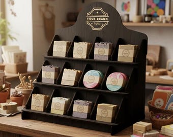 May include: A dark wooden display stand with multiple shelves, showcasing various soaps. The soaps are rectangular and round, with different colors and labels. The top of the stand has the text "YOUR BRAND" in gold lettering.