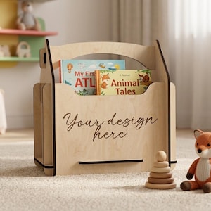 May include: A light-colored wooden book rack with a handle cutout at the top. The front panel features the black cursive text "Your design here". Two children's books titled "My First ATLAS" and "Animal Tales" are visible inside the rack.
