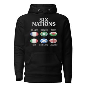 Könnte beinhalten: Schwarzer Kapuzenpullover mit dem Text "SIX NATIONS" und Rugbyball-Grafiken, die Frankreich, Irland, Wales, Italien, Schottland und England darstellen. Der Pullover hat eine Vordertasche und eine Kapuze mit Kordelzug.