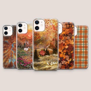 May include: A collection of five phone cases featuring autumn-themed designs. The cases showcase various fall scenes, including a forest with colorful trees, a cozy cottage, and a pattern of falling leaves. The cases are clear with the designs visible.