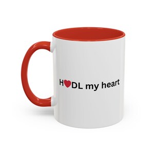 May include: White ceramic mug with a red interior and handle. The mug features the text "H❤️DL my heart" in black, with a red heart symbol. A simple, yet eye-catching design for coffee or tea.