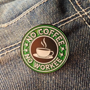 May include: A circular enamel pin with a green border and the words "NO COFFEE NO WORKEE". The centre is brown with a white coffee cup and steam. The pin is set against a denim background.