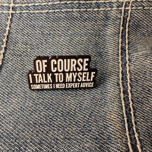 Könnte beinhalten: Ein schwarz-weißer Emaille-Pin mit dem Text "OF COURSE I TALK TO MYSELF SOMETIMES I NEED EXPERT ADVICE" auf einem Jeans-Hintergrund. Der Pin ist rechteckig mit abgerundeten Kanten und einem weißen Rand.