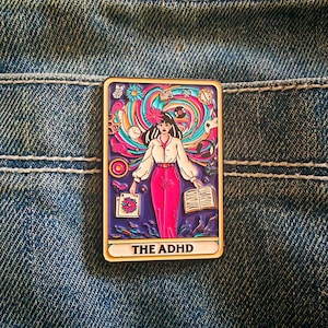 May include: A rectangular enamel pin featuring a central figure in a white shirt and pink trousers, surrounded by colourful swirling patterns, icons like a clock, book, and game controller, with the text THE ADHD printed at the bottom.