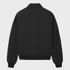 May include: A solid black jacket featuring a pointed collar, long sleeves with ribbed cuffs, and a ribbed hem. The garment has a clean, minimalist design with a small, subtle tonal logo embroidered on the center back of the collar area.