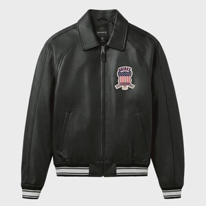May include: Black leather jacket with a collar, zipper closure, and a patch on the chest. The patch features a design with red, white, and blue colors. The jacket has white and black striped cuffs and hem. The brand name "AVIREX" is visible.