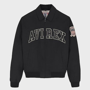 May include: A black zip-up jacket featuring a classic collar and ribbed cuffs. The chest displays the text AVI REX in large, arched, white-outlined black lettering. A patch on the left sleeve features an American flag and the text AVIREX.