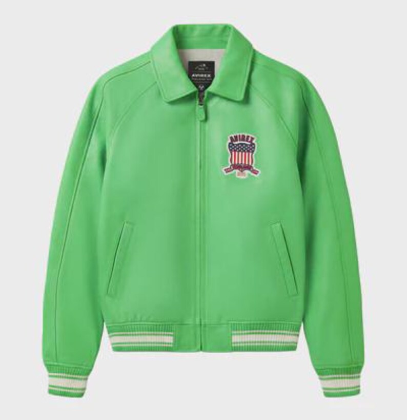 K&ouml;nnte beinhalten: Leuchtend gr&uuml;ne Lederjacke mit Kragen und Rei&szlig;verschluss. Sie hat einen Brustaufn&auml;her mit patriotischem Design und wei&szlig;-gr&uuml;n gestreifte B&uuml;ndchen und Saum. Die Jacke hat zwei Vordertaschen.