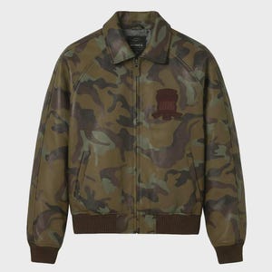 May include: A camouflage print leather jacket featuring a full-length front zipper, a classic collar, and ribbed knit cuffs and hem. The chest displays a dark brown embroidered patch with the text Avirex. The jacket has two side pockets.