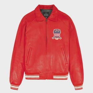 May include: A vibrant red leather jacket with a classic collar and a full-zip closure. The jacket features a patch with an American flag design on the chest. The cuffs and hem have white stripes. A stylish outerwear piece.