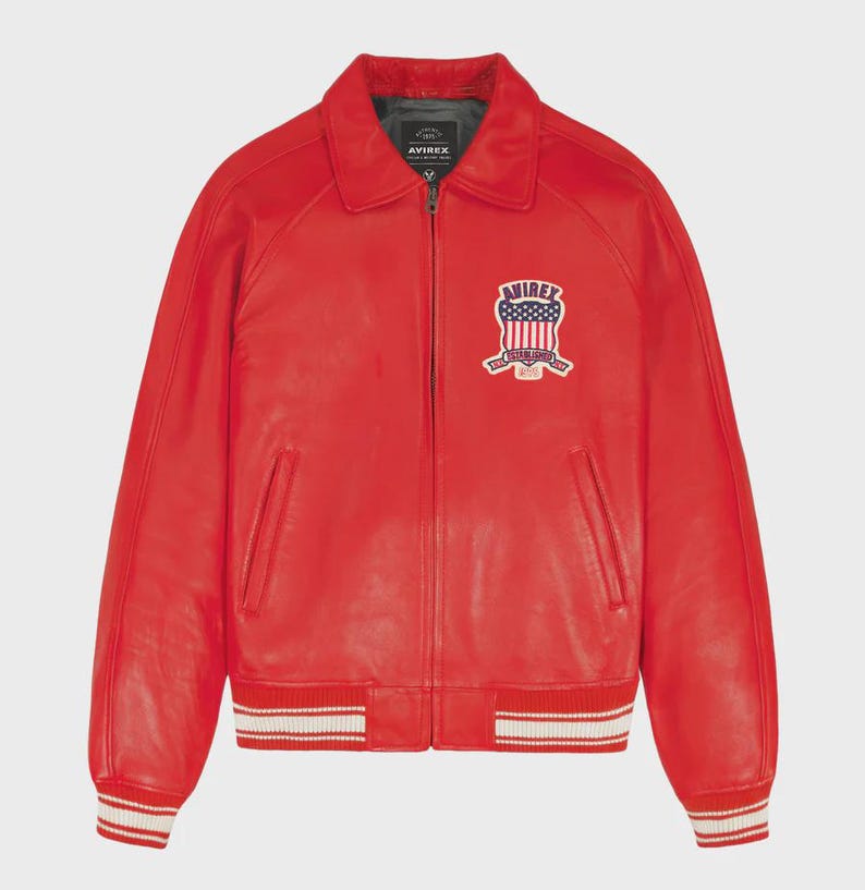 May include: A vibrant red leather jacket with a classic collar and a full-zip closure. The jacket features a patch with an American flag design on the chest. The cuffs and hem have white stripes. A stylish outerwear piece.