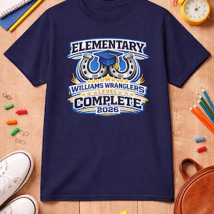 May include: Navy blue t-shirt with a graphic for elementary school graduation. The design includes the text "ELEMENTARY", "WILLIAMS WRANGLERS", "LEVEL", "COMPLETE", and the year "2026". The design features a graduation cap and horseshoes.