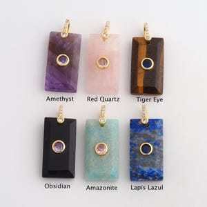 May include: Six rectangular gemstone pendants with gold-colored bails. The gemstones include amethyst, red quartz, tiger eye, obsidian, amazonite, and lapis lazuli. Each pendant has a smaller, circular gemstone in the center, and the names of the gemstones are printed below.