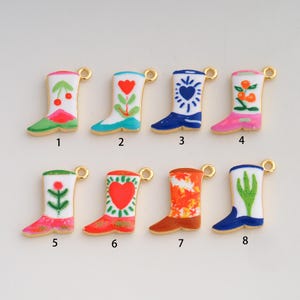 May include: Eight metal charms shaped like cowboy boots, each featuring unique enamel designs including cherries, flowers, hearts, and cacti. Each charm has a small loop at the top for attachment, numbered one through eight for identification.