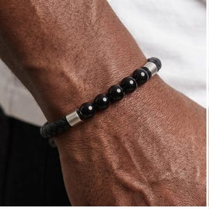 Peut inclure: Bracelet noir avec des perles et un bracelet en cuir tressé. Le bracelet est orné de perles noires polies et d'éléments métalliques argentés. Un accessoire élégant porté au poignet.