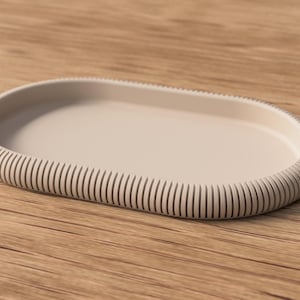 Op de afbeelding: Een beige, ovaalvormige schaal met een geribbelde rand. De schaal is gemaakt van een stevig materiaal en staat op een houten oppervlak. De geribbelde rand voegt een decoratief element toe aan het ontwerp van de schaal.