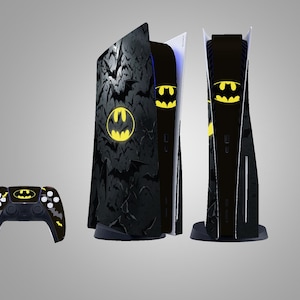 Puede incluir: Una consola de juegos y un mando con temática de Batman en negro y amarillo. La consola presenta un logotipo de Batman amarillo y siluetas de murciélagos. El mando tiene un diseño a juego. La consola mide unos 38 cm de alto.