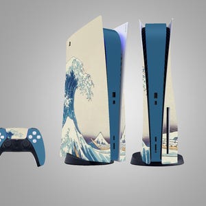 Op de afbeelding: Een gameconsole en controller set met een blauw en beige ontwerp geïnspireerd op het Japanse kunstwerk "De grote golf van Kanagawa". De console heeft een blauw midden en de controller heeft een bijpassend ontwerp.