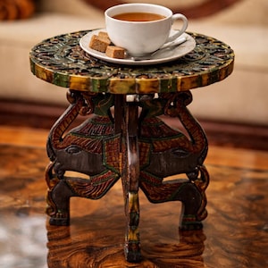 May include: A small, round wooden side table with intricate carvings and elephant-shaped legs. The tabletop is adorned with a white teacup, saucer, and sugar cubes. The table is painted with green, gold, and red accents, and is approximately 18 inches in diameter.
