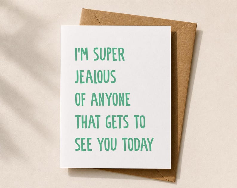 Peut inclure: Une carte de v&oelig;ux blanche avec le texte "I'M SUPER JEALOUS OF ANYONE THAT GETS TO SEE YOU TODAY" en lettres vertes, plac&eacute;e sur une enveloppe marron. La carte et l'enveloppe sont pos&eacute;es sur un fond neutre.
