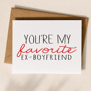 May include: A white greeting card with the text "YOU'RE MY favorite EX-BOYFRIEND" in black and red font, placed on top of a brown envelope. The card is square-shaped and the font is a mix of serif and script.