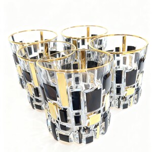 May include: Set of five clear drinking glasses with a geometric design. The glasses feature a pattern of black and gold rectangles and squares. Each glass has a gold rim.